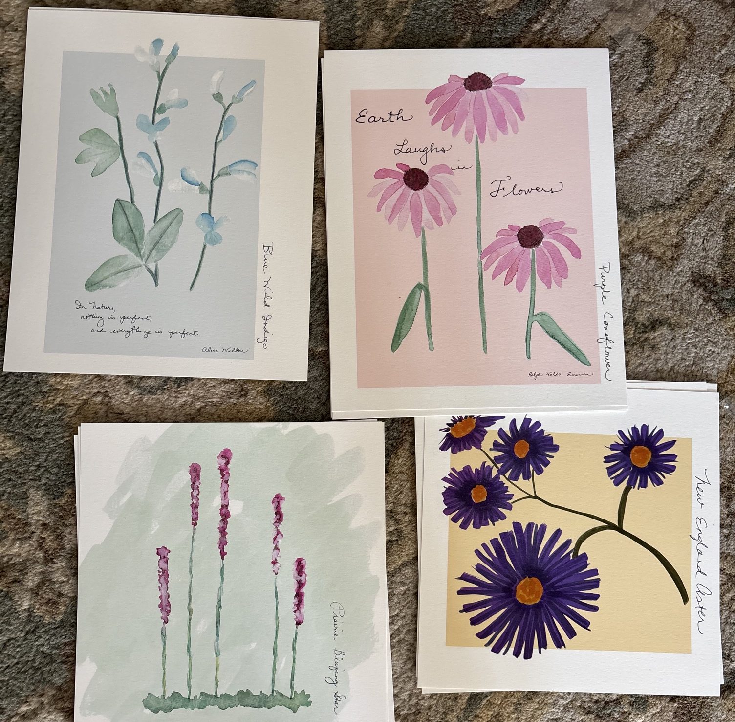 A collection of four floral art prints featuring watercolor illustrations of various flowers. Each print has a different background color and includes handwritten titles such as 'Blue Wild Sage', 'Earth Laughs in Flowers', 'Purple Coneflower', and 'Queen Bee's Blessing'.